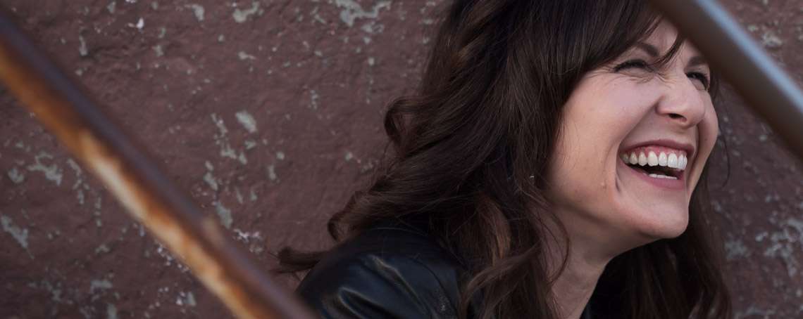 Jacquie Drew smiling outside, sitting on a staircase