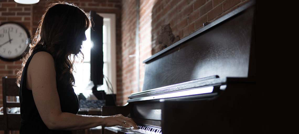 Jacquie Drew playing a piano in the Tenato Strategy office