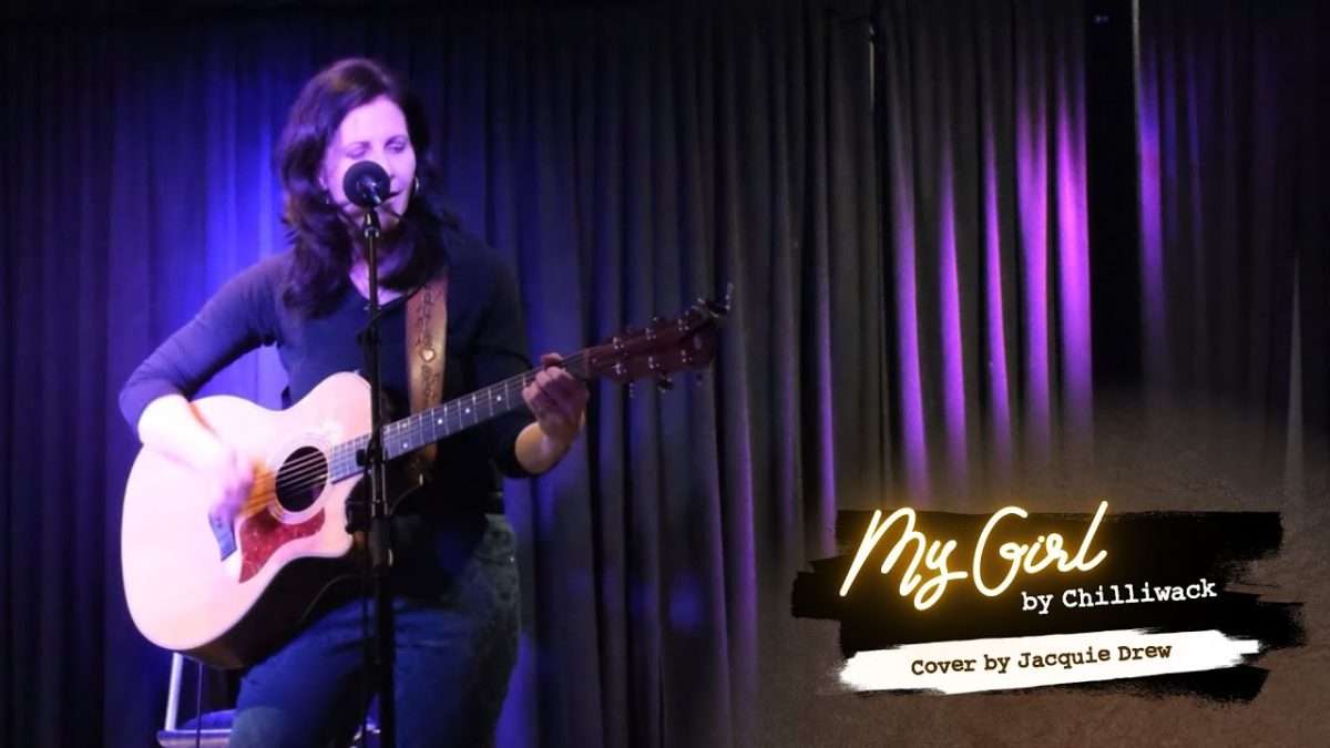 Jacquie Drew playing guitar and singing during a live performance
