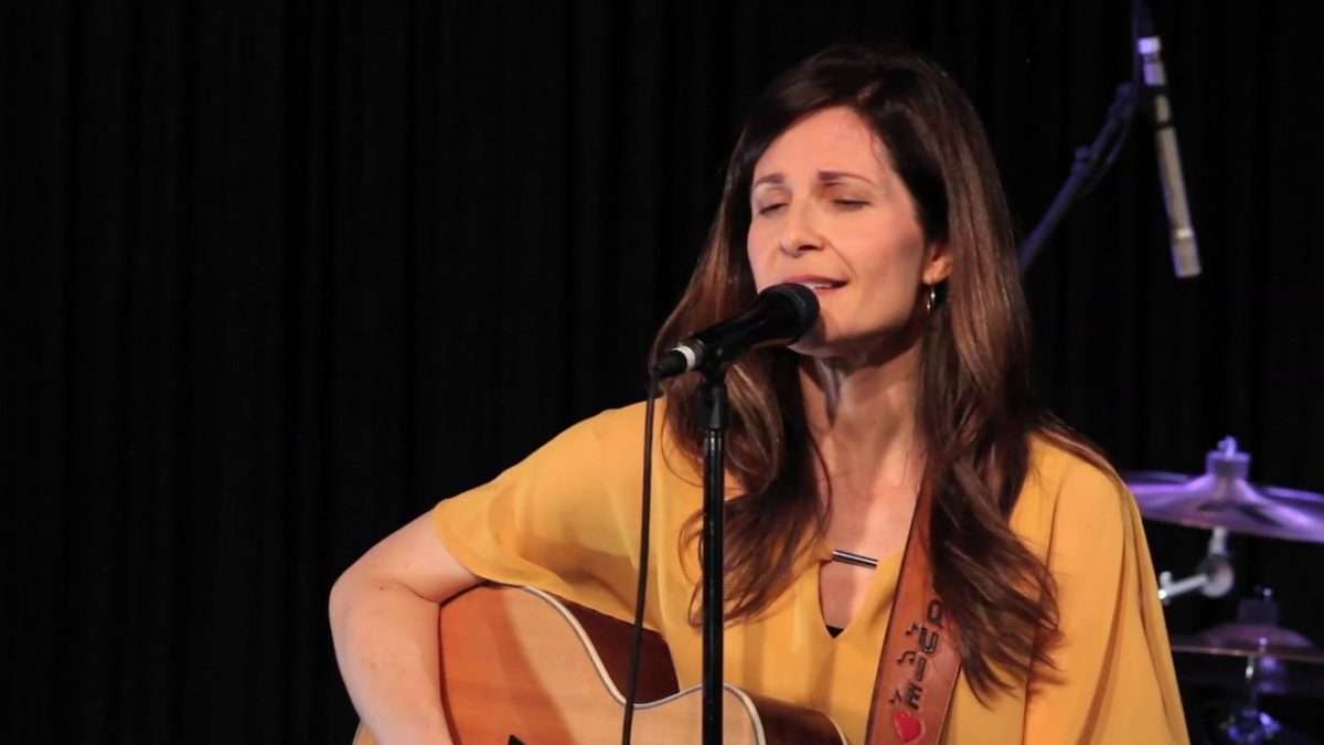Jacquie Drew playing guitar and singing during a live performance